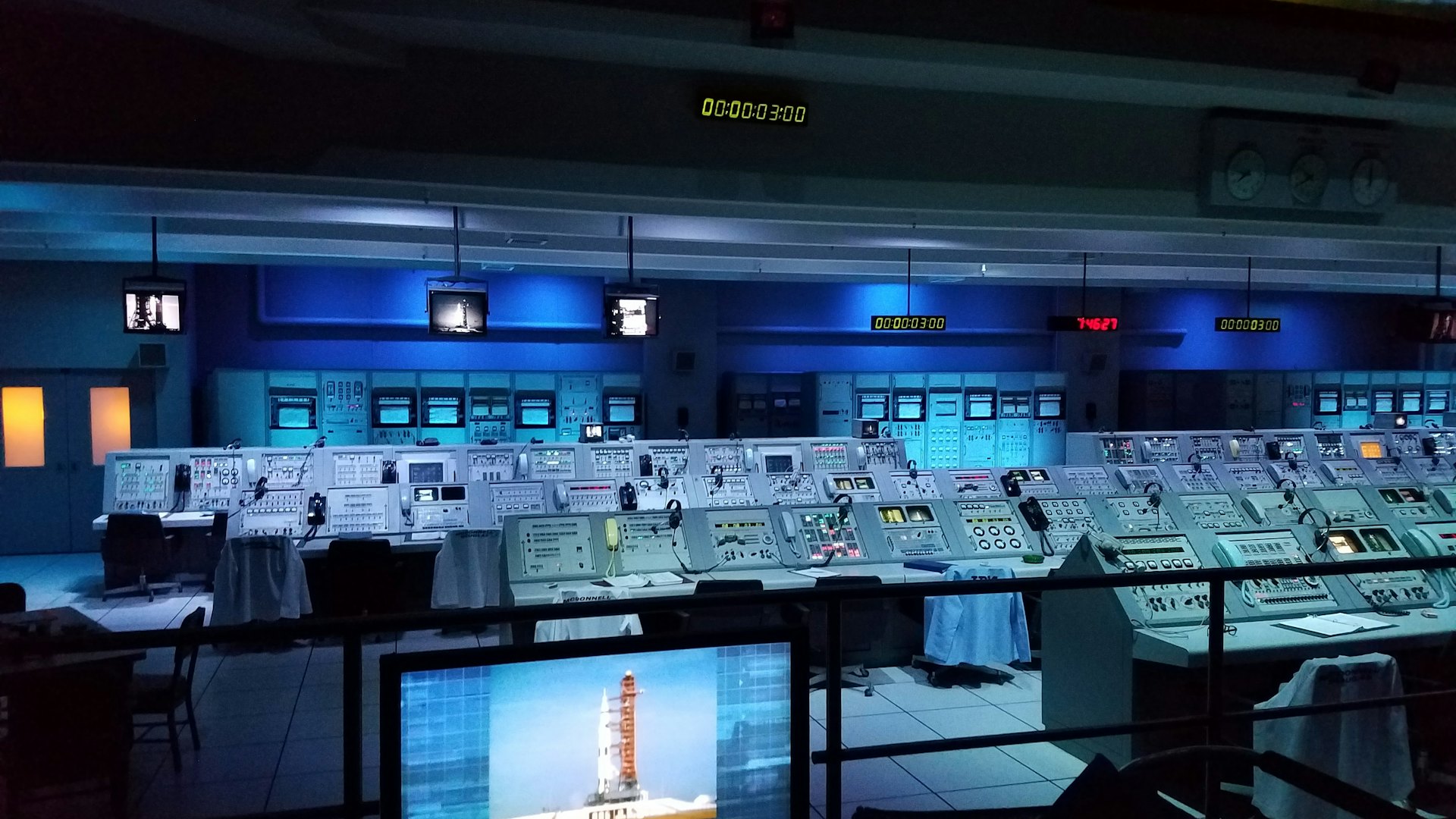 Dimly lit launch control room with rows of consoles receding into the distance
